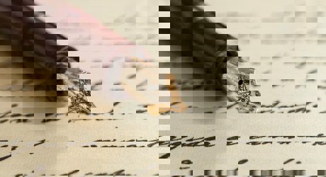 A sheet of paper with black handwriting on which rests the nib and first half of a brown fountain pen