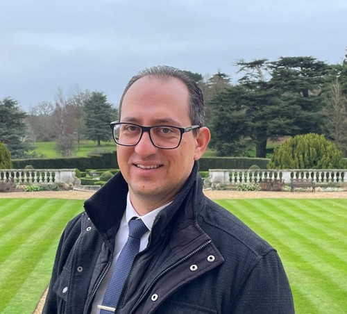 man with glasses a coat and tie stood in front of a lawn