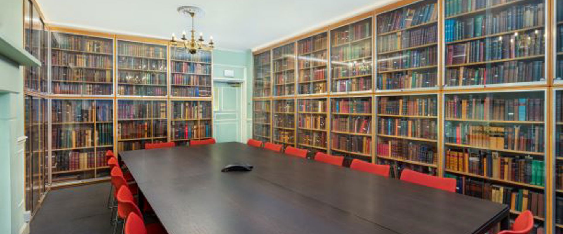 large dark wood table with red chairs around it with walls lined with bookshelves in the background