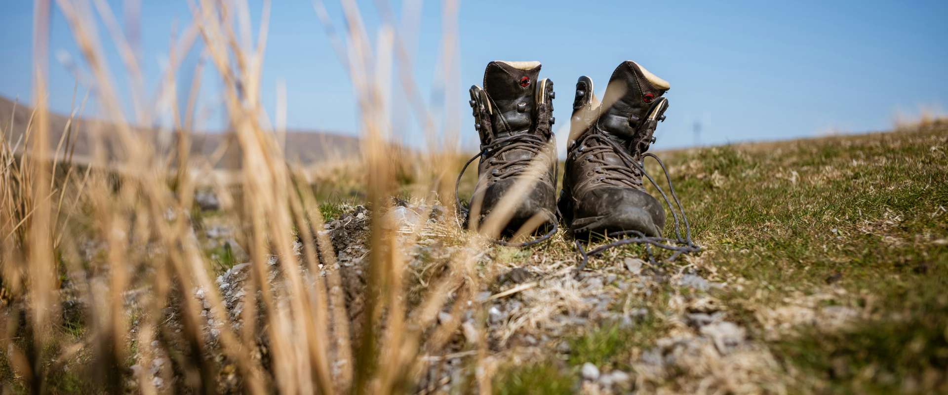A pair of walking boots on the grass next to some rocks, with blue sky in the background