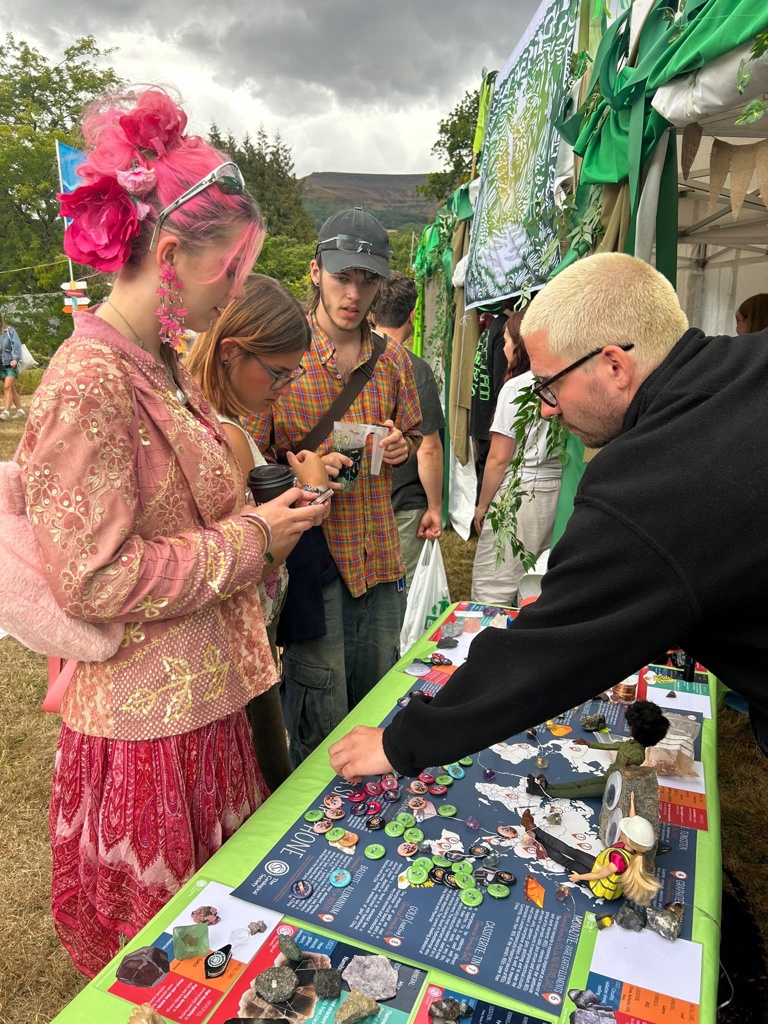 Three young people interactive with a geology outreach stand and staff member, with a table full of informative posters, badges and minerals