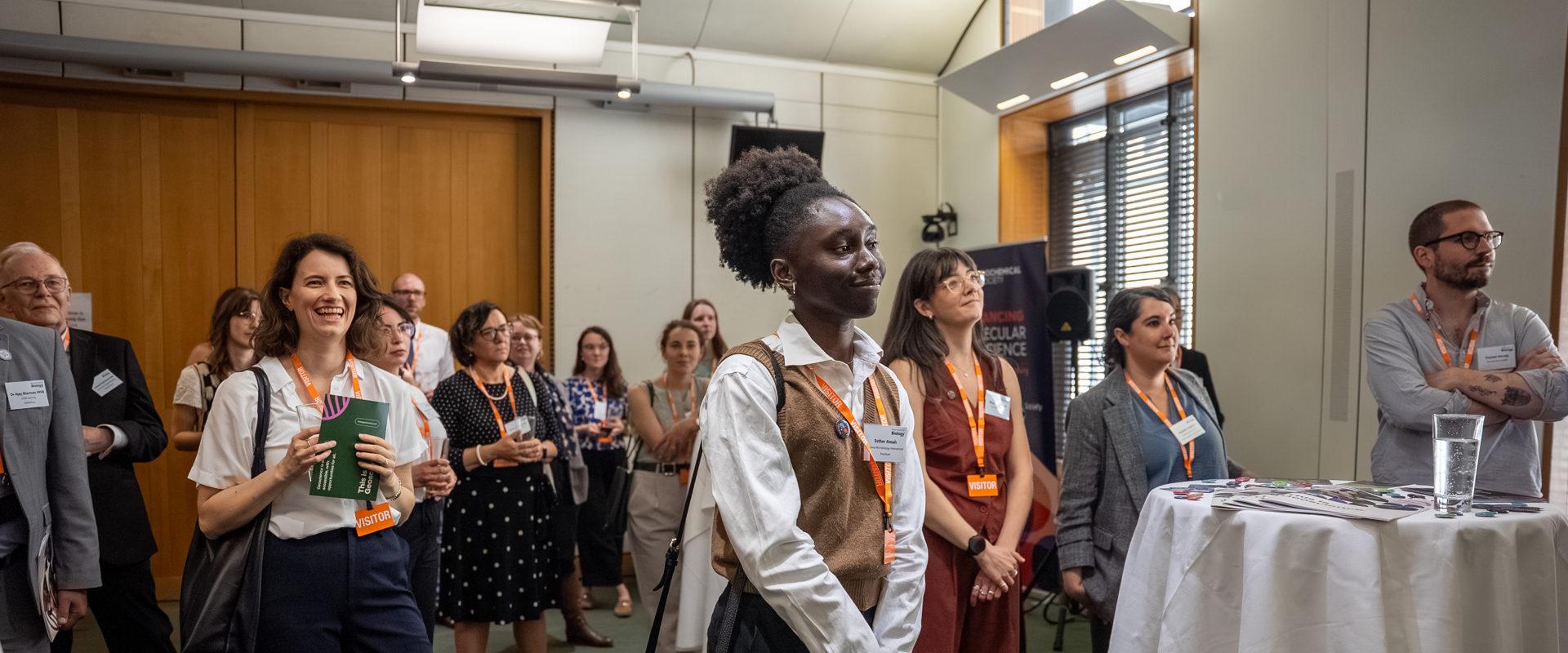 People with lanyards and name badges in a room listening to someone speak