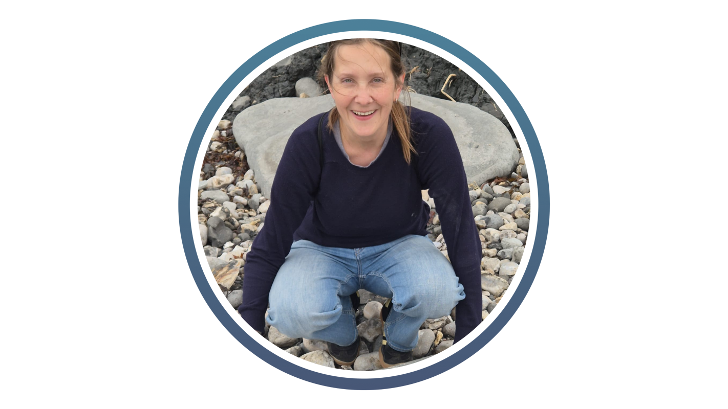 white woman with a blue jumper and blue jeans kneeling down on some pebbles whilst smiling