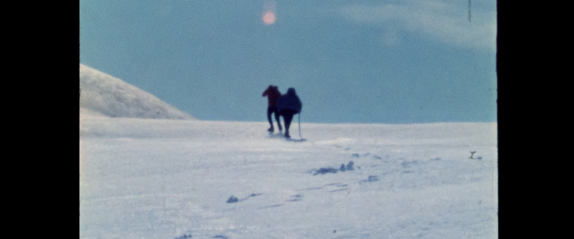 Two people hike up slope in glacier.