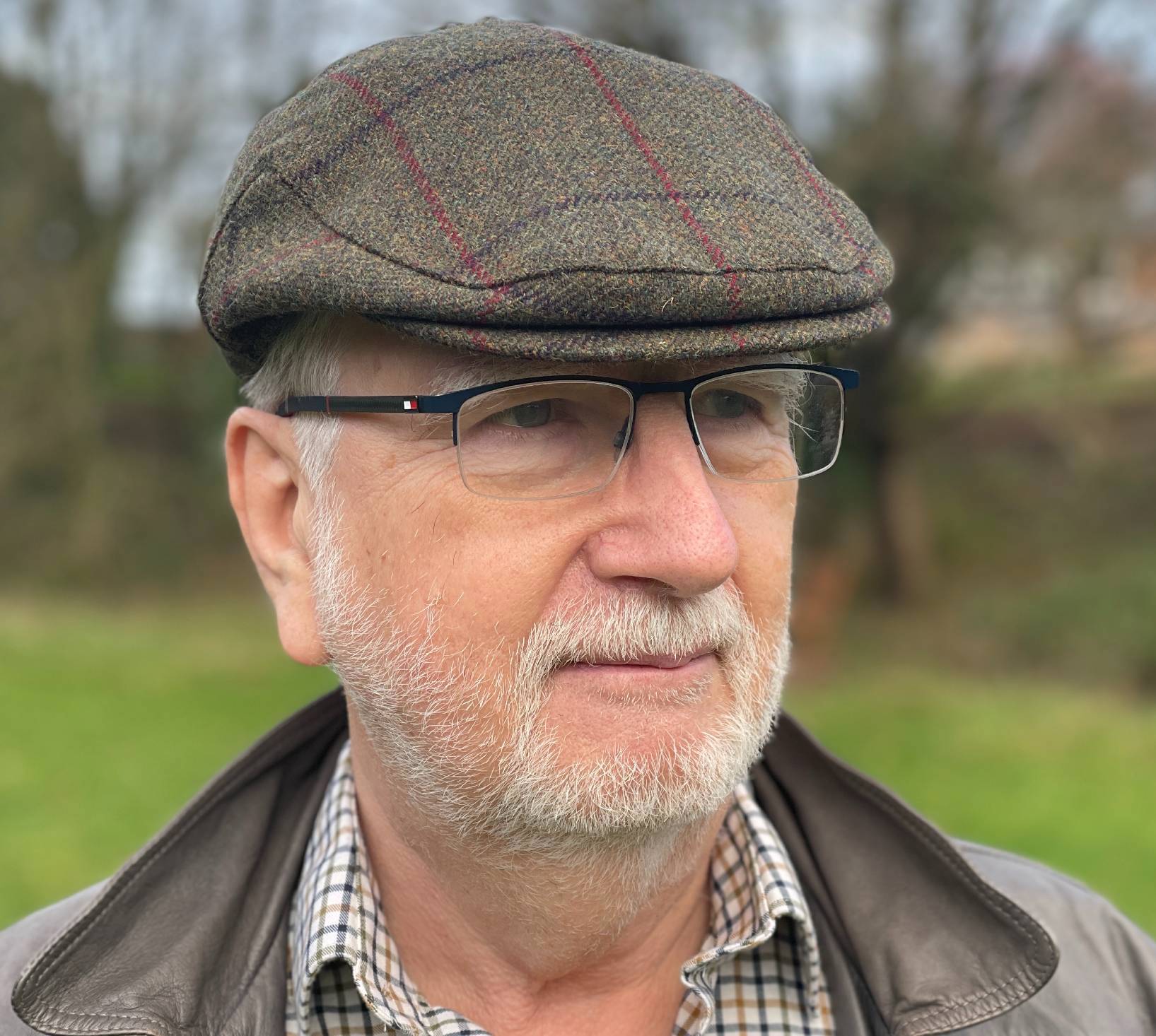 white man with glasses wearing a checked tweed cap, checked shirt and brown jacket
