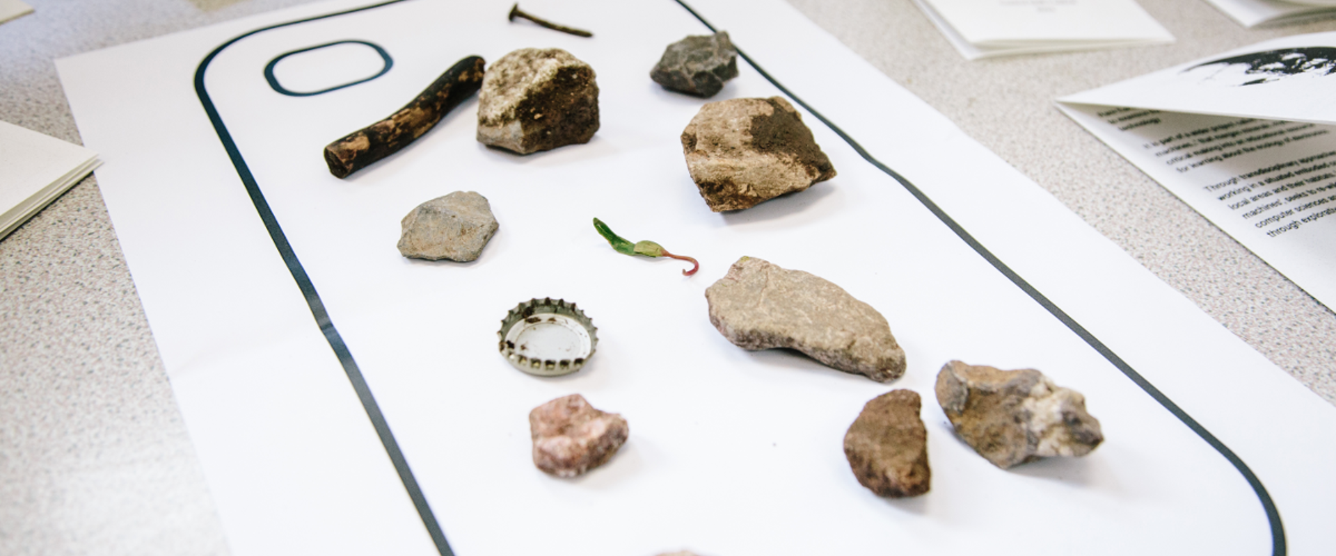 Rocks, old, rust bottle cap and nail laid out on a piece of paper. 