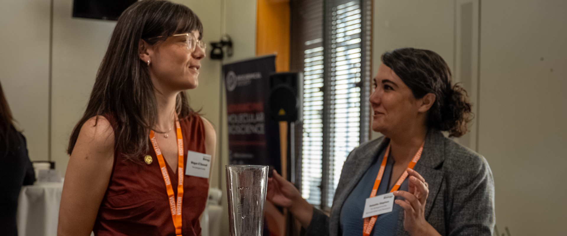 Two women smiling and discussing in front of a table with geoscience booklets, postcards and badges. 