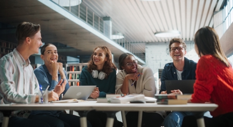 A group of young people around a table with laptops and textbooks laughing