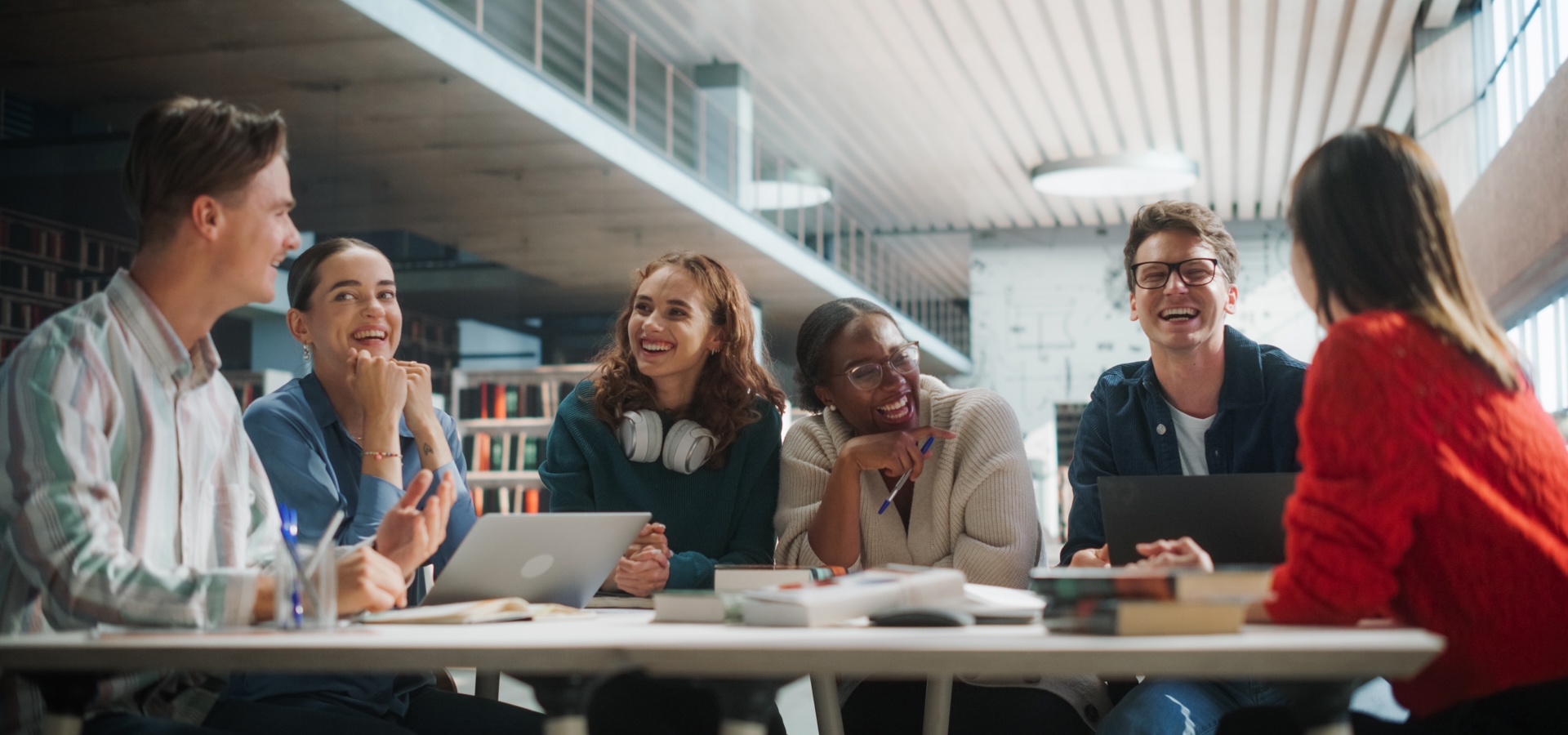 A group of young people around a table with laptops and textbooks laughing