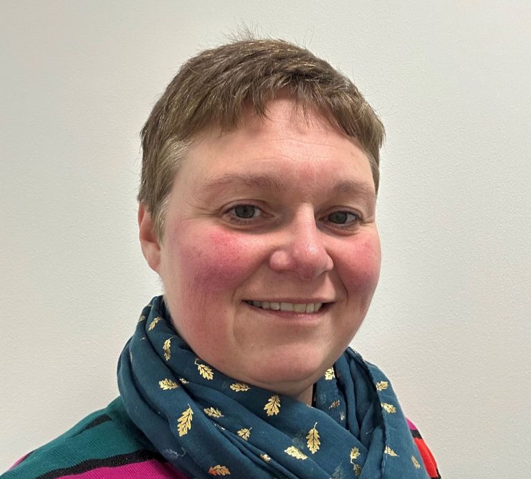 woman with short hair wearing a blue and gold scarf and a pink top
