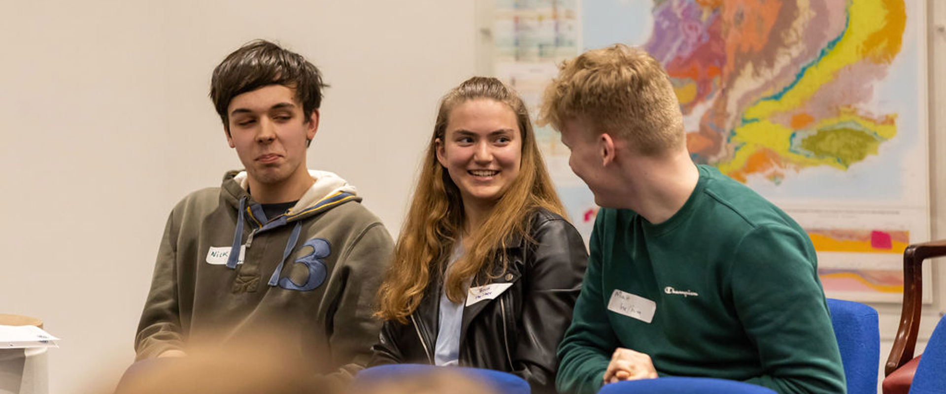 Three students smiling and laughing at a theatre with a map on the background