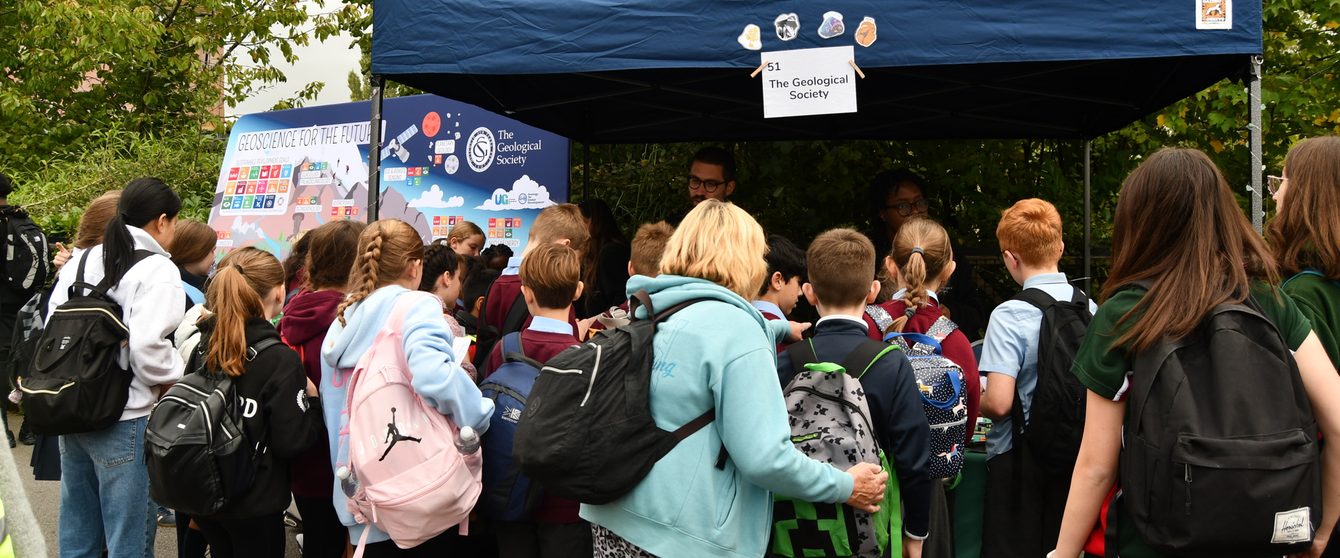 a group of young children, some in school uniform, looking at  a market stall with the geological society written above it