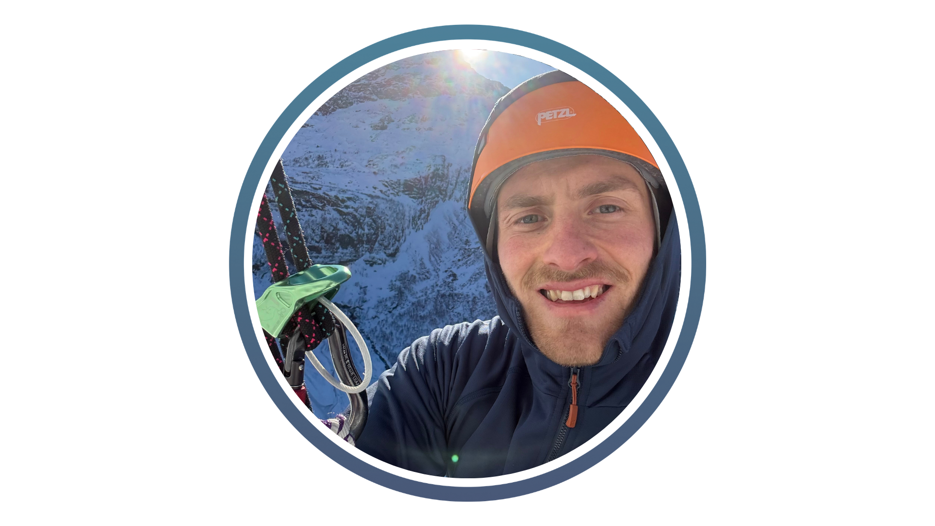 Climber wearing an orange helmet and blue jacket with snowy mountain and bright sun in the background.