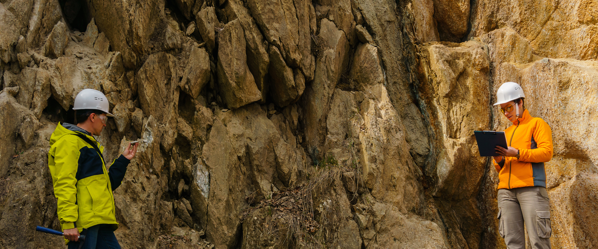 two people in high vis jackets and hard hats inspecting a rocky area