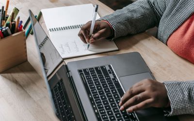 Person taking an online course and writing down notes on a notebook