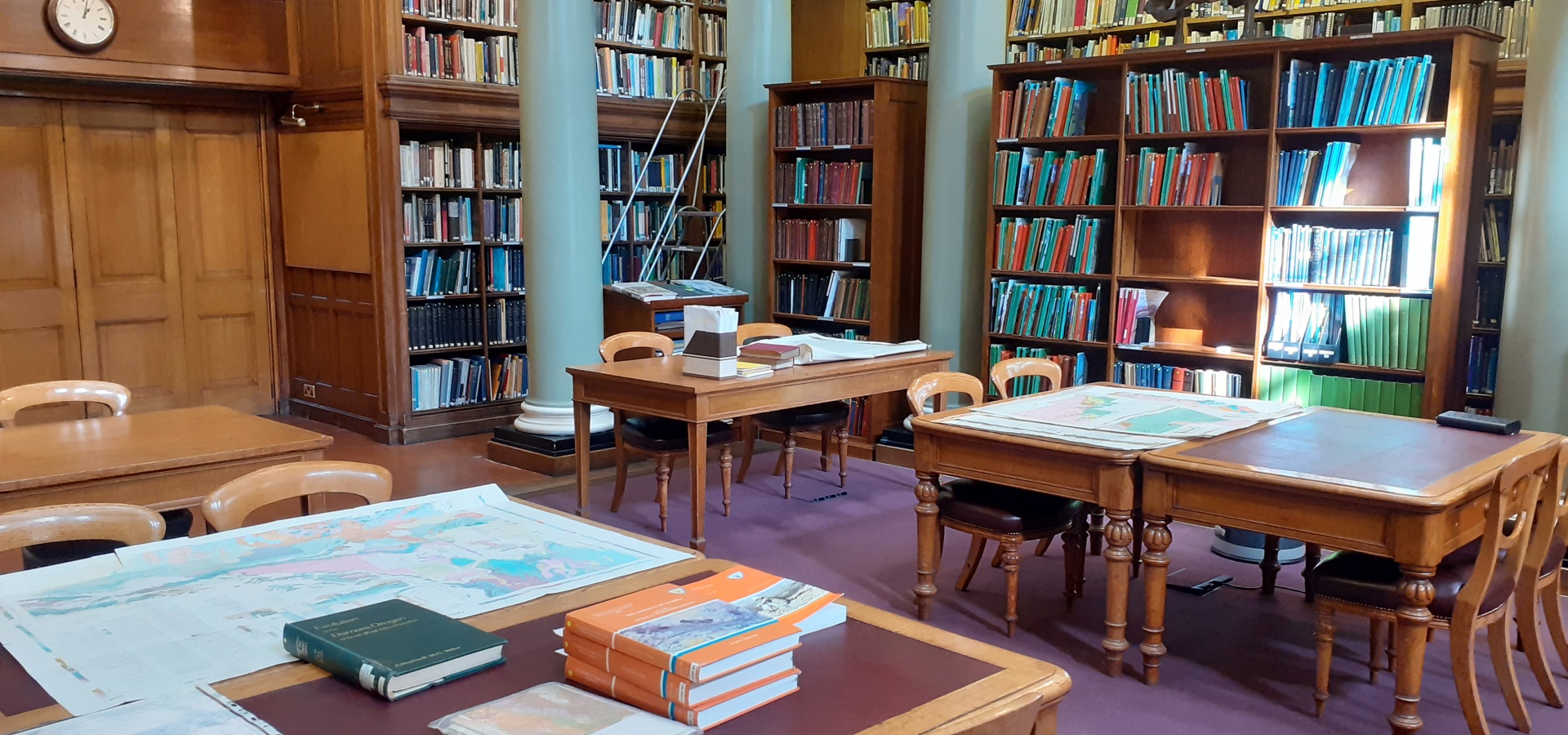 Upper Library of the Geological Society, with books and maps on wooden tables, with sunlight falling on them