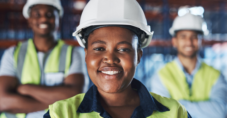 Woman with hard hat smiling with two men either side of her