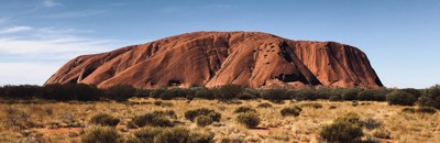 huge red rock mountain (Uluru) in background surrounded by dry desert