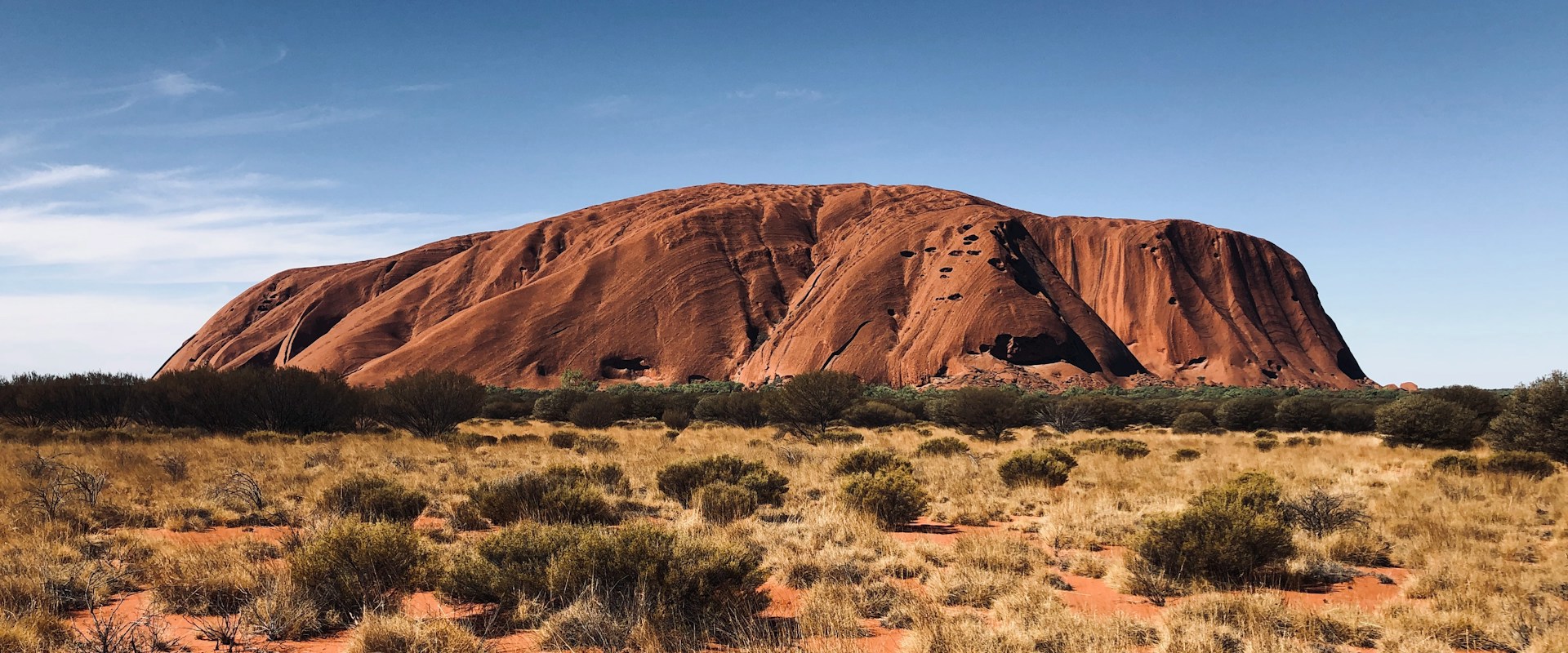 huge red rock mountain (Uluru) in background surrounded by dry desert