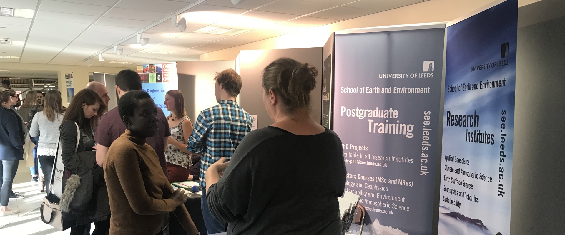 white woman speaking to a black woman at an event stand with postgraduate training on a banner behind them