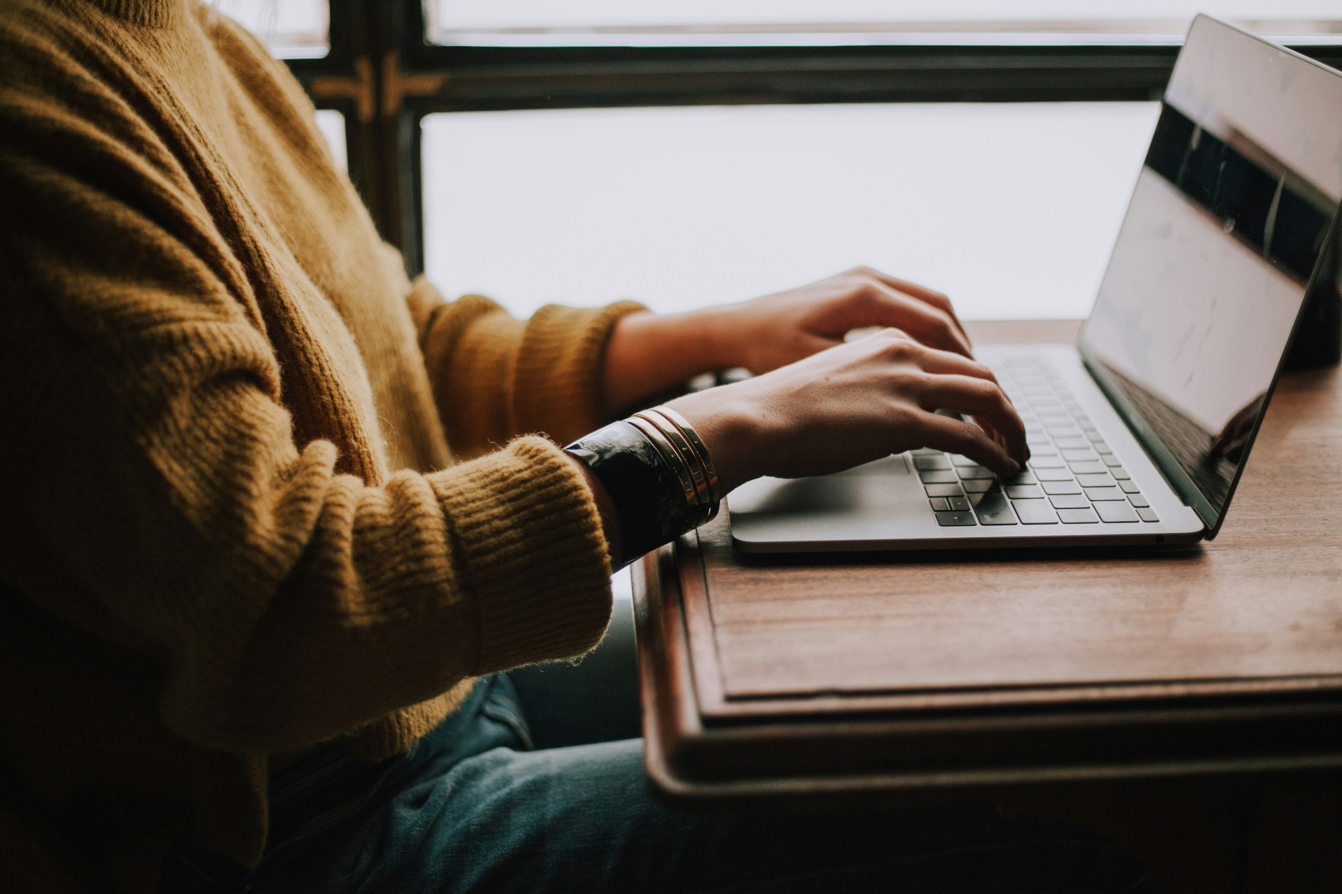 close up of a persons arms and hands tapping onto a laptop keyboard