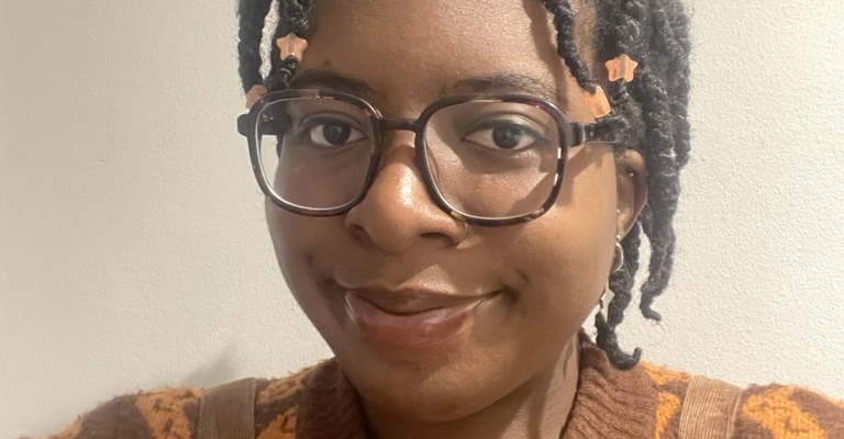 young black woman wearing glasses and a brown and orange jumper