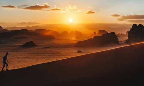 silhouette of a man walking up a hill with the sun in the background
