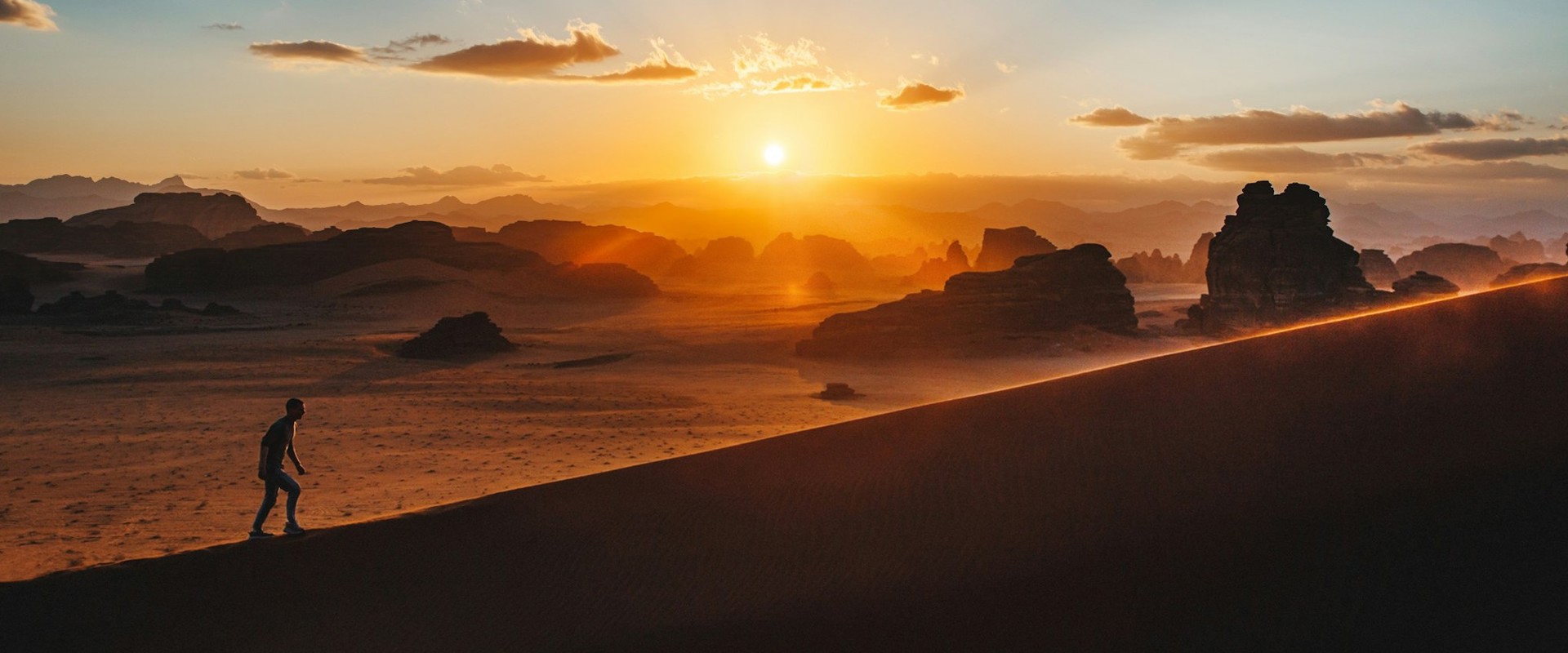 silhouette of a man walking up a hill with the sun in the background