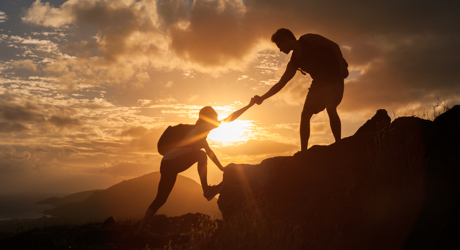 a person reaching out to another person to help them climb up a rocky mountain