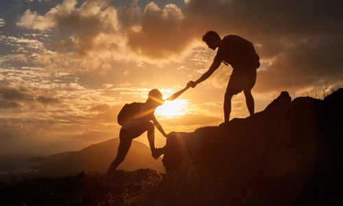 a person reaching out to another person to help them climb up a rocky mountain