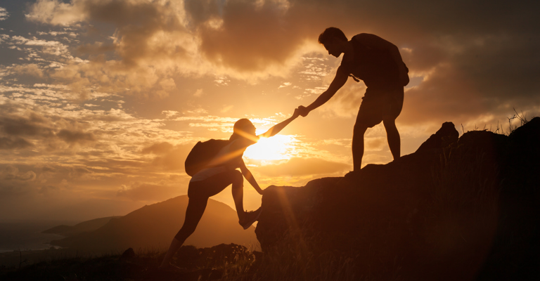 a person reaching out to another person to help them climb up a rocky mountain