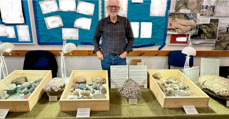 man stood behind a table which has boxes of rocks on it